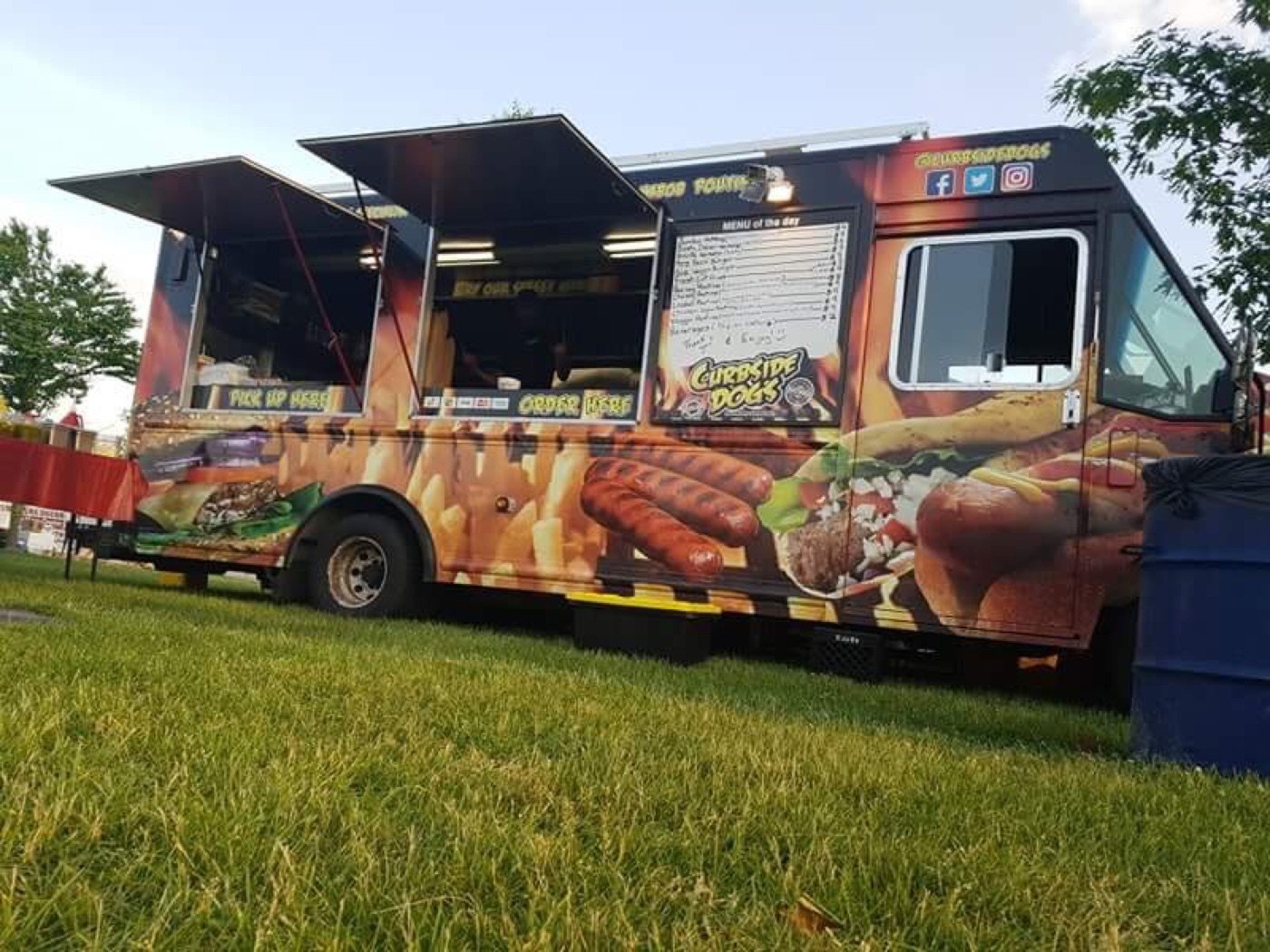 Curbsidedogs truck open for service on a grass lot at dusk